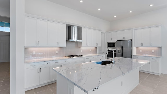 kitchen with wall chimney exhaust hood, white cabinetry, stainless steel appliances, and a kitchen island with sink