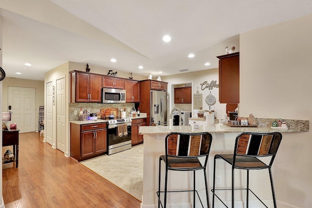 kitchen with backsplash, a kitchen breakfast bar, light hardwood / wood-style floors, kitchen peninsula, and stainless steel appliances