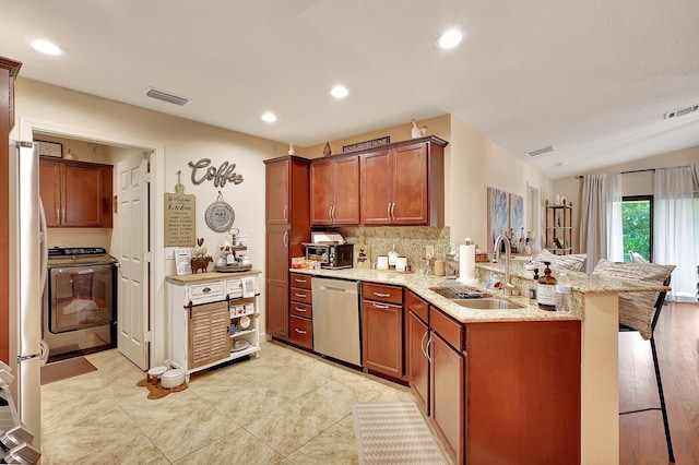 kitchen featuring kitchen peninsula, light stone counters, a breakfast bar, stainless steel appliances, and sink