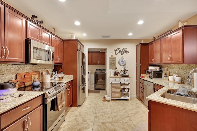 kitchen with backsplash, sink, washer and dryer, light stone counters, and stainless steel appliances