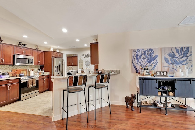 kitchen with a kitchen breakfast bar, decorative backsplash, light wood-type flooring, kitchen peninsula, and stainless steel appliances