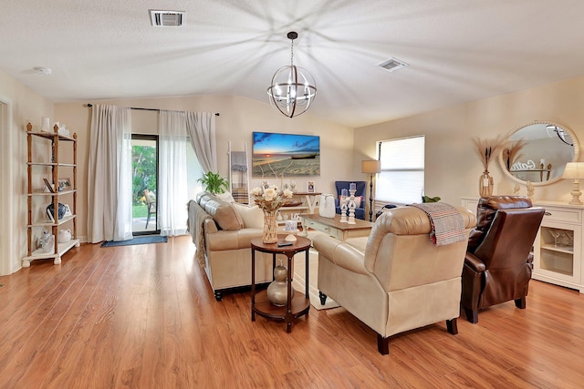 living room featuring a textured ceiling, light hardwood / wood-style floors, lofted ceiling, and a notable chandelier