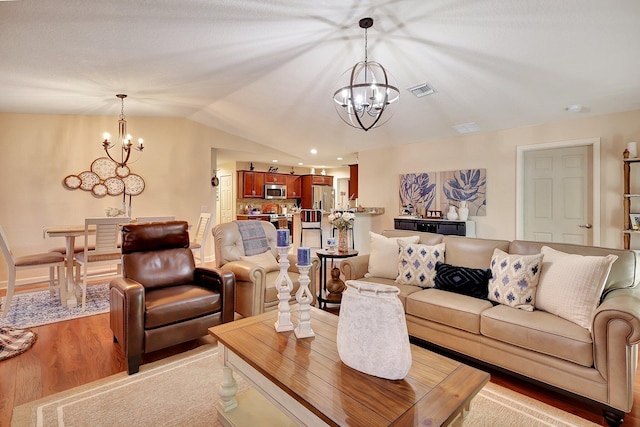 living room with light hardwood / wood-style flooring, vaulted ceiling, and an inviting chandelier