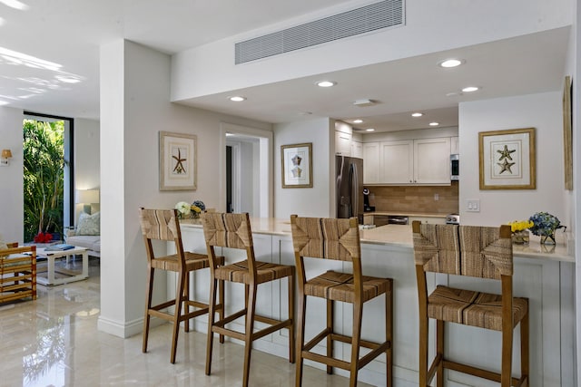 kitchen featuring a kitchen breakfast bar, kitchen peninsula, appliances with stainless steel finishes, tasteful backsplash, and white cabinetry