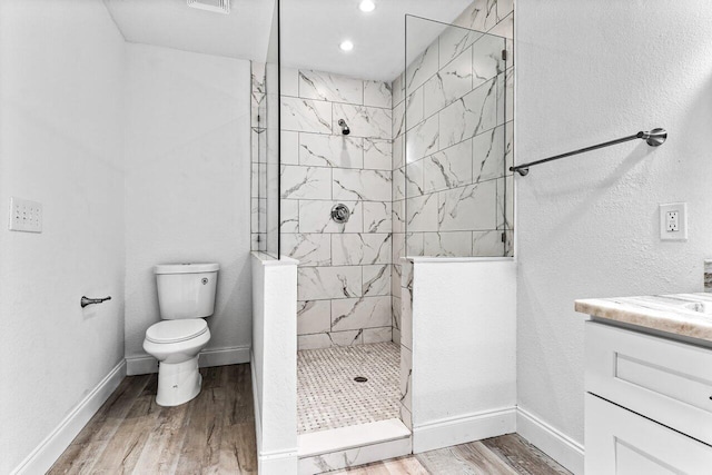 bathroom featuring vanity, toilet, a tile shower, and wood-type flooring