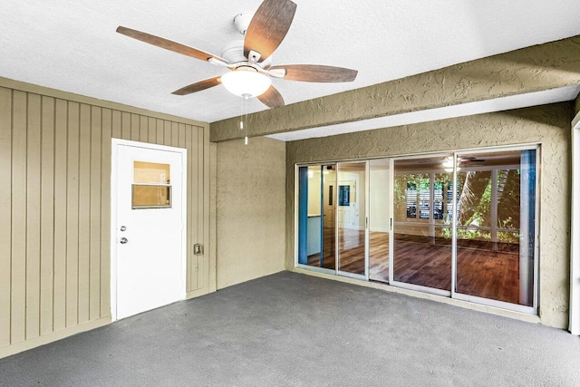 carpeted spare room with a textured ceiling, ceiling fan, and wooden walls