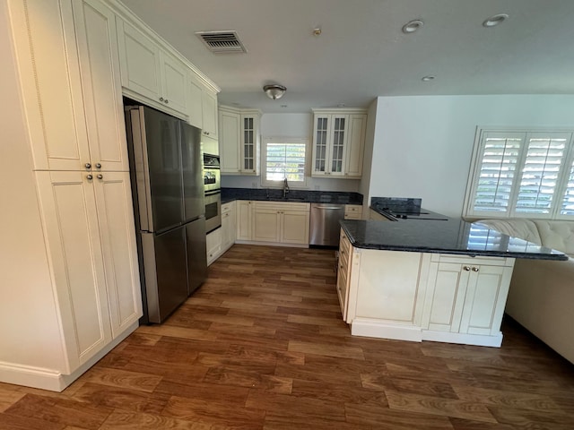 kitchen featuring kitchen peninsula, stainless steel appliances, dark wood-type flooring, sink, and white cabinetry