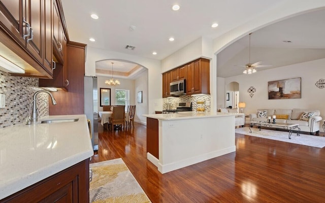 kitchen featuring decorative backsplash, appliances with stainless steel finishes, kitchen peninsula, ceiling fan with notable chandelier, and dark wood-type flooring