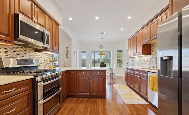 kitchen with hanging light fixtures, sink, appliances with stainless steel finishes, light hardwood / wood-style floors, and kitchen peninsula