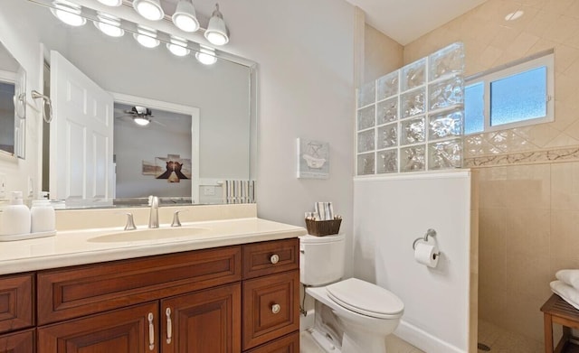 bathroom featuring ceiling fan, toilet, a tile shower, and vanity