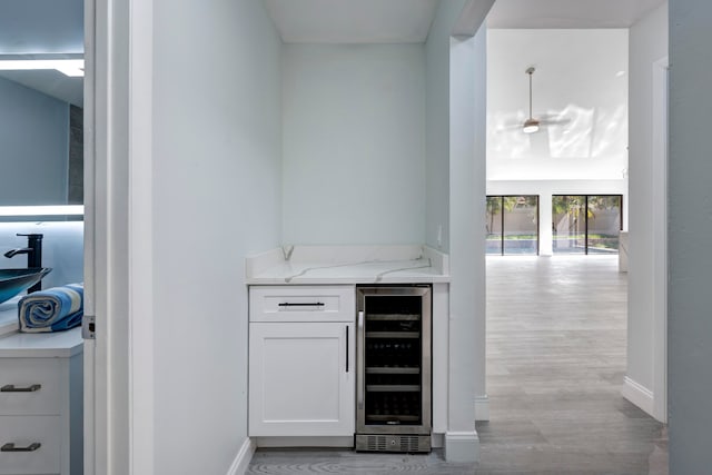 bar featuring white cabinets, sink, wine cooler, light wood-type flooring, and light stone countertops