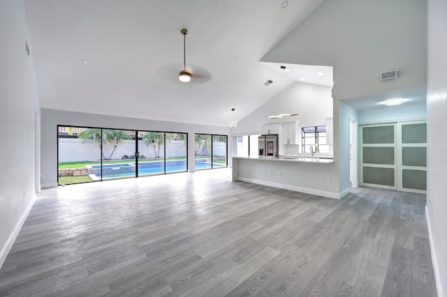 unfurnished living room with light wood-type flooring, sink, and high vaulted ceiling