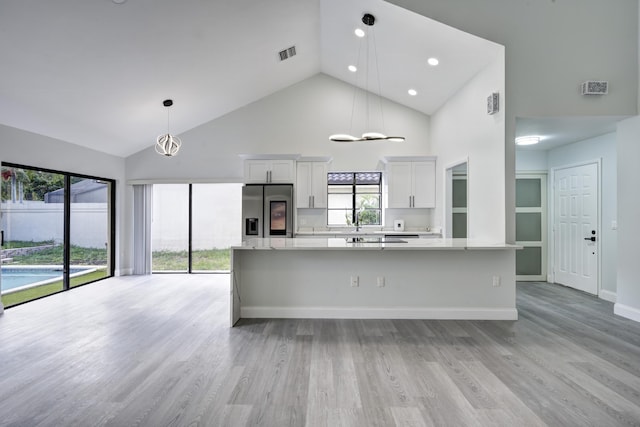 kitchen featuring high vaulted ceiling, stainless steel refrigerator with ice dispenser, hanging light fixtures, light wood-type flooring, and white cabinetry