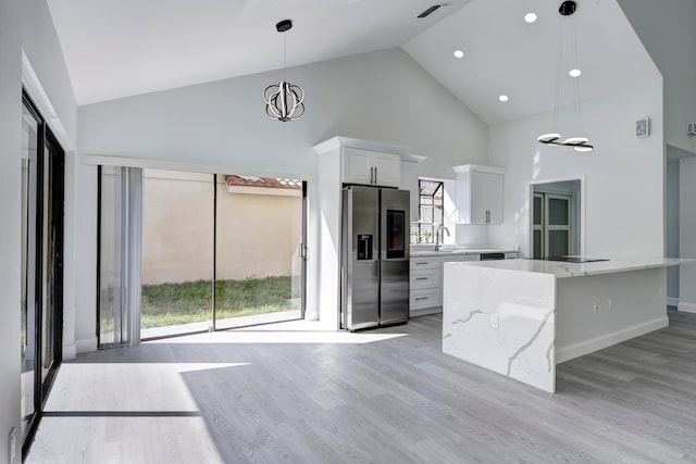 kitchen with stainless steel fridge, decorative light fixtures, high vaulted ceiling, a center island, and white cabinetry