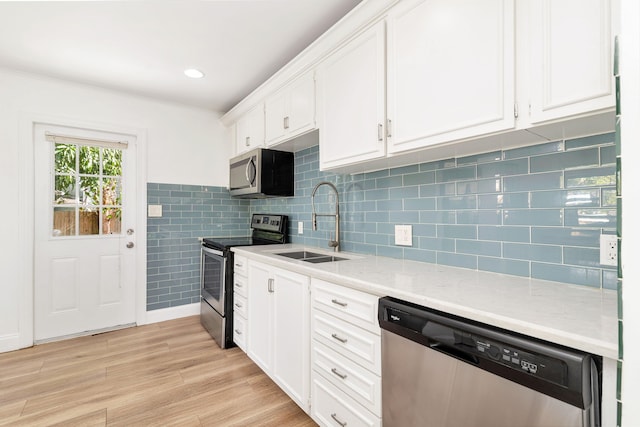 kitchen with appliances with stainless steel finishes, light stone counters, sink, light hardwood / wood-style floors, and white cabinetry