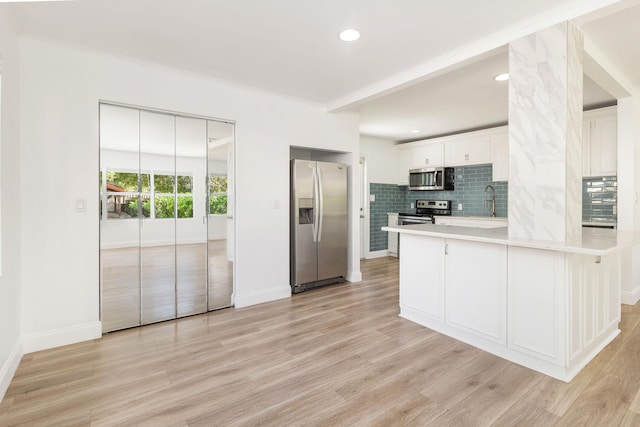 kitchen featuring white cabinetry, kitchen peninsula, crown molding, light hardwood / wood-style floors, and appliances with stainless steel finishes