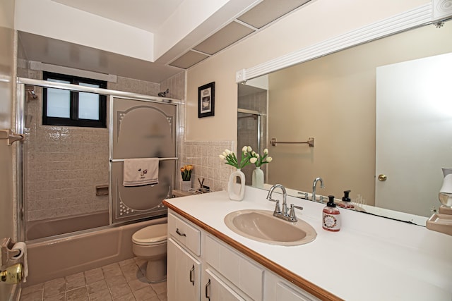 full bathroom with combined bath / shower with glass door, tile patterned floors, vanity, tile walls, and toilet