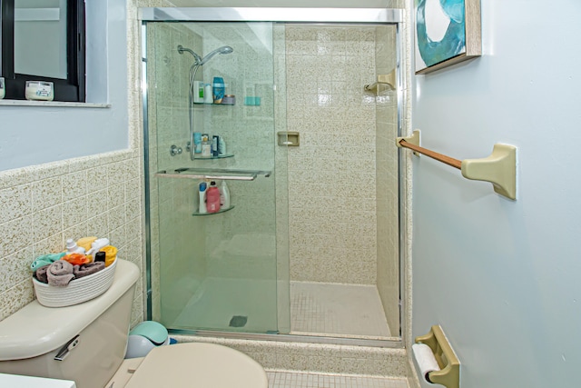 bathroom with a shower with shower door, tile walls, and toilet