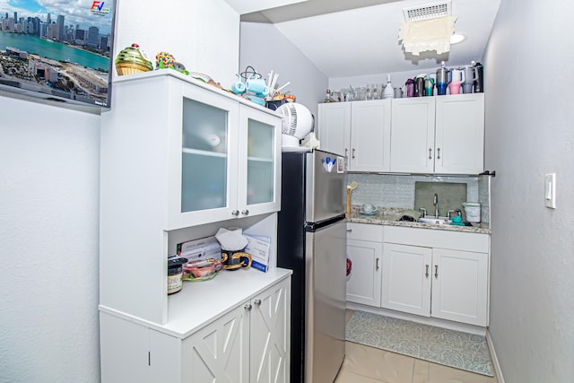 kitchen with decorative backsplash, white cabinetry, stainless steel refrigerator, and sink