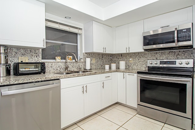 kitchen with sink, light tile patterned floors, appliances with stainless steel finishes, light stone counters, and white cabinetry