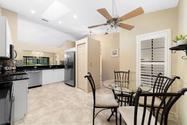 tiled dining space with ceiling fan with notable chandelier, sink, and vaulted ceiling with skylight