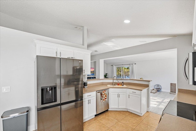 kitchen with appliances with stainless steel finishes, a textured ceiling, vaulted ceiling, sink, and white cabinetry