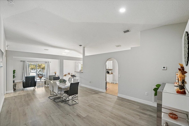 dining area with a textured ceiling, light wood-type flooring, and vaulted ceiling