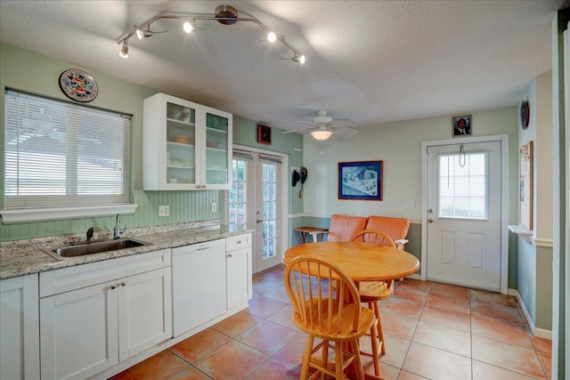 kitchen featuring light stone countertops, a textured ceiling, white dishwasher, light tile patterned floors, and white cabinets