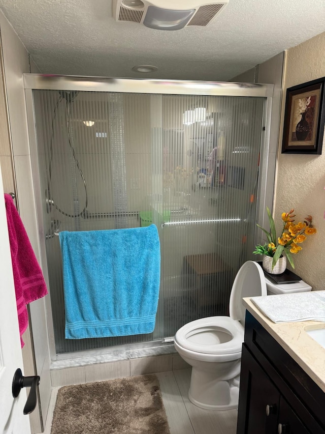 bathroom featuring vanity, a textured ceiling, toilet, and a shower with door