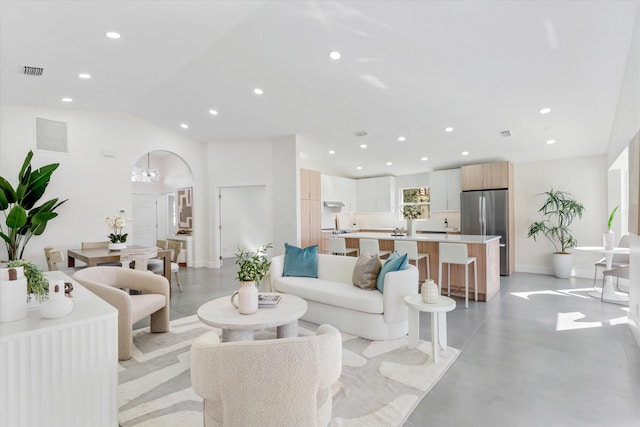 living area with arched walkways, recessed lighting, visible vents, finished concrete flooring, and vaulted ceiling