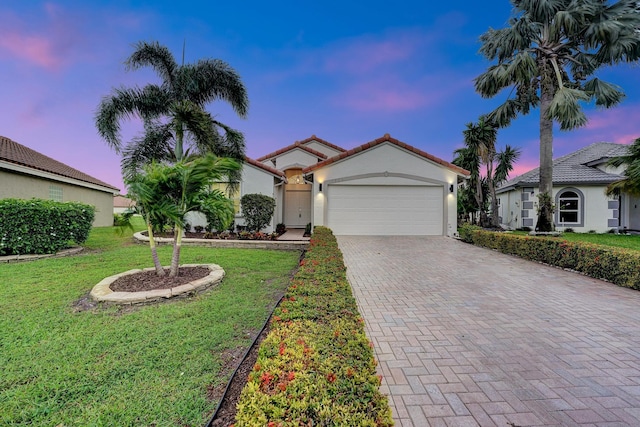 mediterranean / spanish-style house with decorative driveway, a yard, stucco siding, an attached garage, and a tiled roof