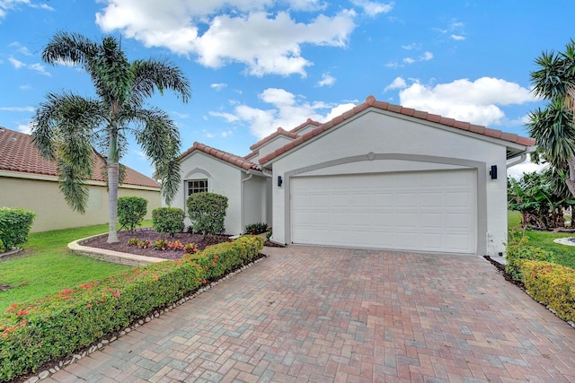 mediterranean / spanish house with a garage, a tiled roof, decorative driveway, and stucco siding