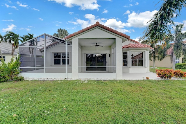 back of house with a tile roof, glass enclosure, ceiling fan, and a lawn