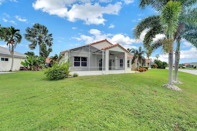 rear view of property featuring glass enclosure, ceiling fan, and a yard