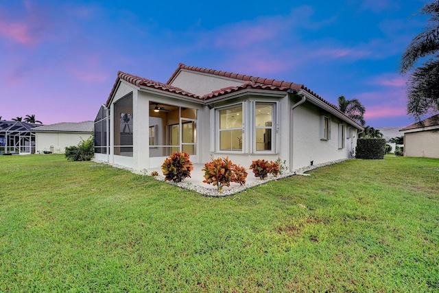 back of property with a tiled roof, a lawn, and stucco siding