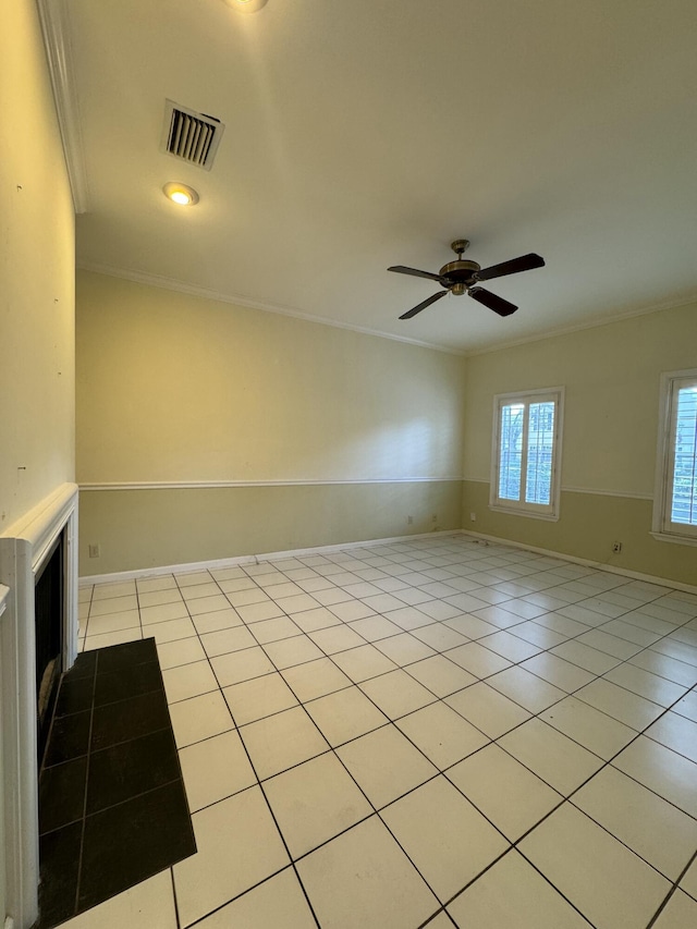 tiled spare room featuring ceiling fan, ornamental molding, and a fireplace