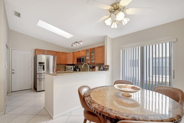 tiled dining room with lofted ceiling with skylight, ceiling fan, and sink