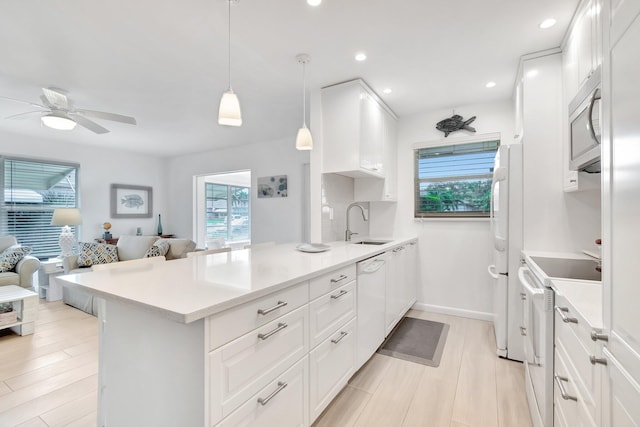 kitchen with pendant lighting, white appliances, white cabinets, sink, and light hardwood / wood-style floors