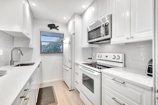 kitchen with white appliances, white cabinets, sink, tasteful backsplash, and light stone counters