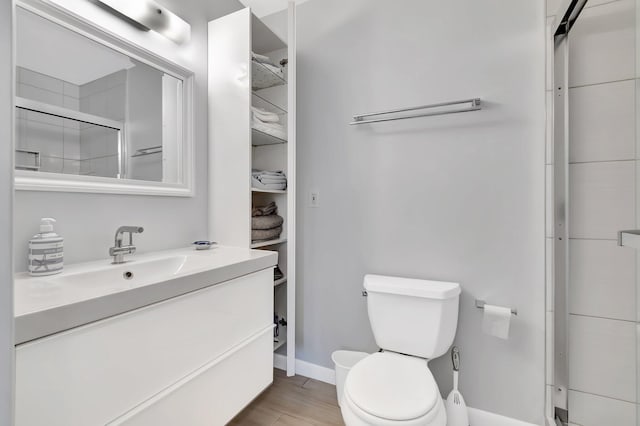 bathroom with wood-type flooring, vanity, toilet, and a shower with door