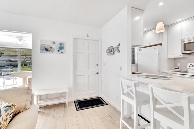 interior space with backsplash, white appliances, ceiling fan, pendant lighting, and white cabinets