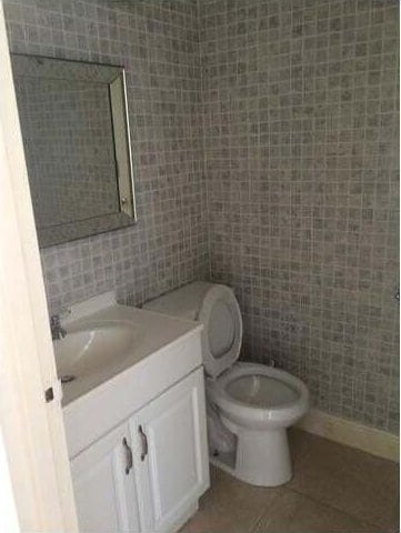 bathroom with tile patterned flooring, vanity, toilet, and tile walls