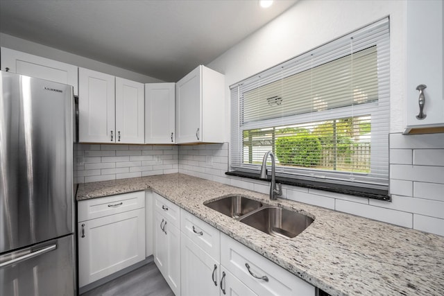 kitchen with stainless steel refrigerator, white cabinetry, sink, light stone countertops, and backsplash