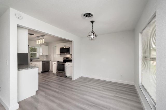 kitchen with pendant lighting, white cabinets, light wood-type flooring, appliances with stainless steel finishes, and tasteful backsplash