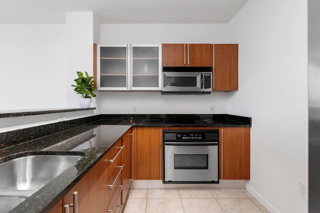 kitchen featuring sink, light tile patterned floors, stainless steel appliances, and dark stone counters