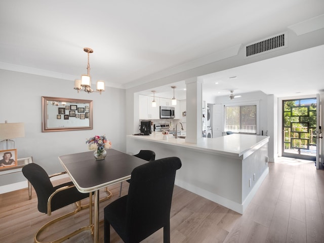 dining space featuring ceiling fan with notable chandelier, sink, crown molding, stacked washer / drying machine, and light hardwood / wood-style floors