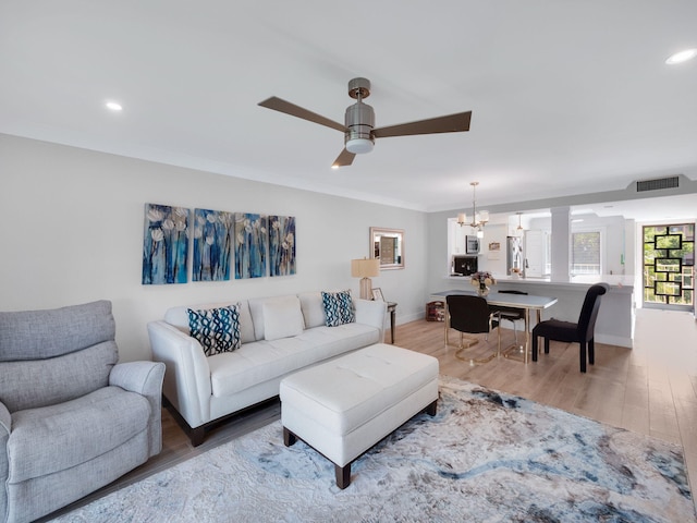 living room with ceiling fan with notable chandelier, hardwood / wood-style flooring, and crown molding