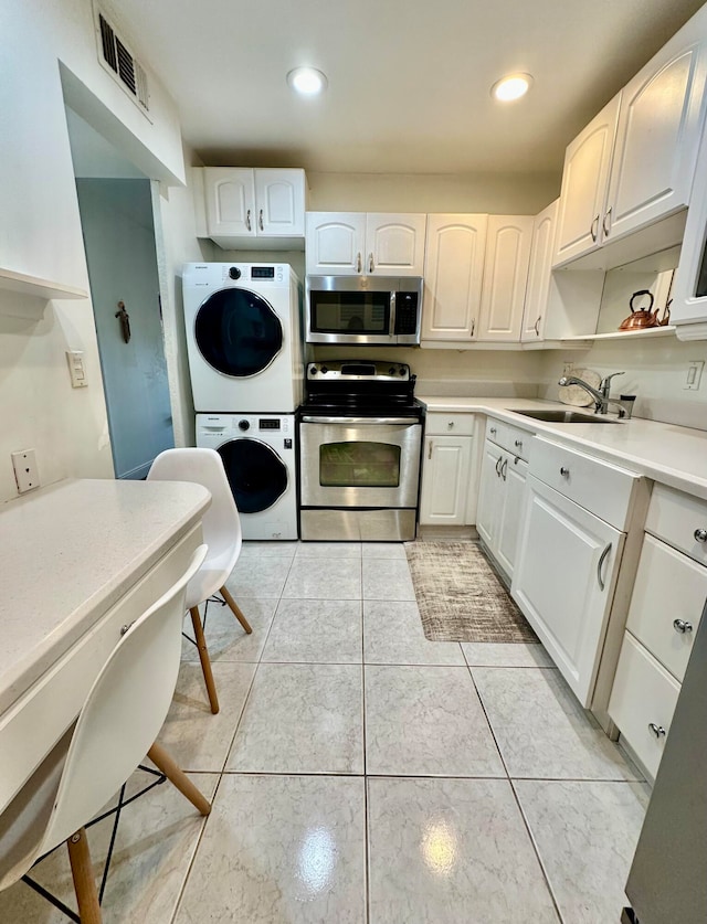 kitchen with appliances with stainless steel finishes, sink, light tile patterned floors, stacked washer and dryer, and white cabinetry