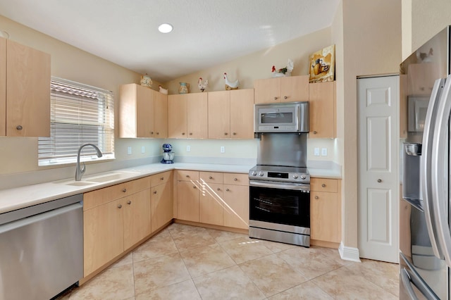 kitchen with light brown cabinets, sink, stainless steel appliances, and vaulted ceiling