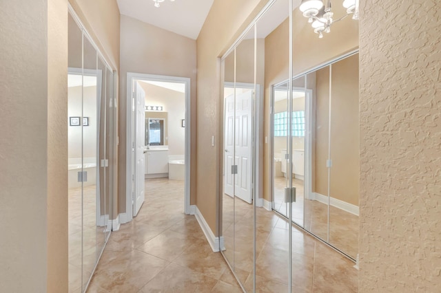 corridor with a chandelier, light tile patterned floors, and vaulted ceiling